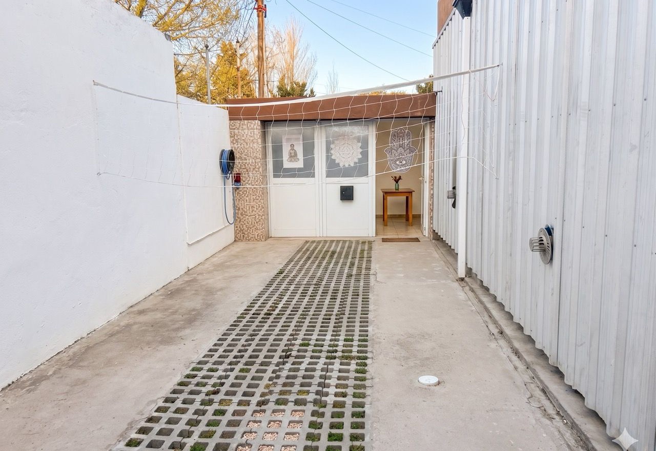 Entrada vehicular lateral hacia el patio y la vivienda del fondo